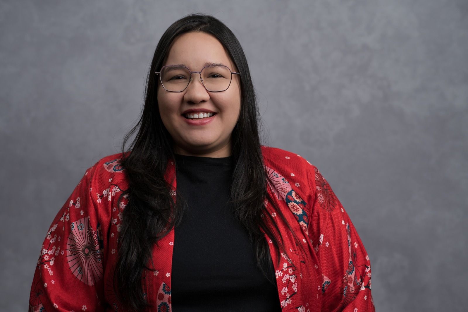 Fotografia de Giu Murakami, uma mulher nipobrasileira de cabelos compridos e lisos, e corpo gordo. Ela sorri para a camera.