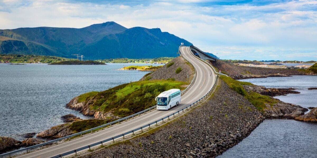a bus driving down a beautiful scenic road over water