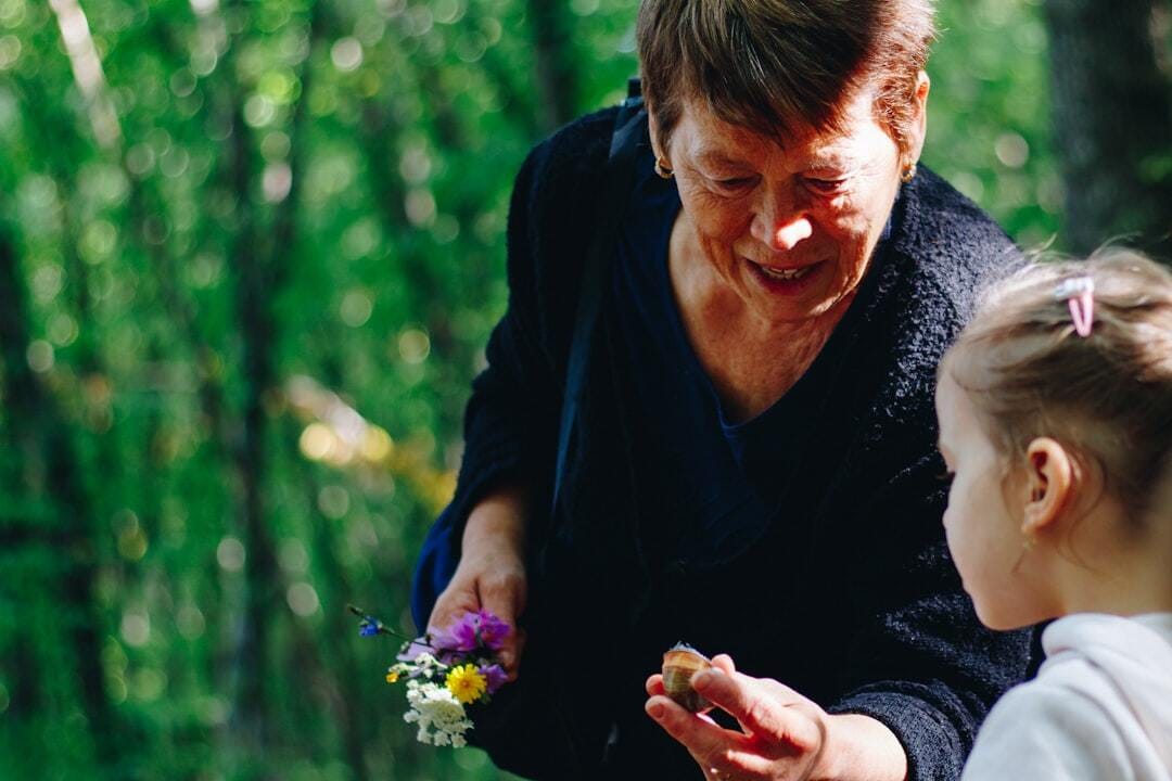 Grandmother is holding a boquet of freshly picked flowers and showing her granduaghter an acorn