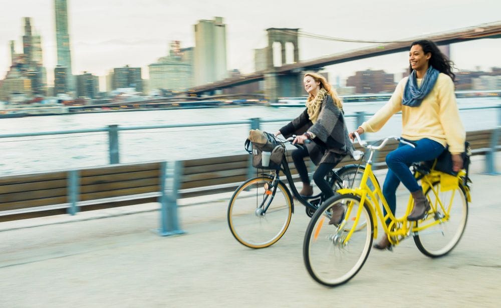 two women biking down a city street with the Brooklyn Bridge in view