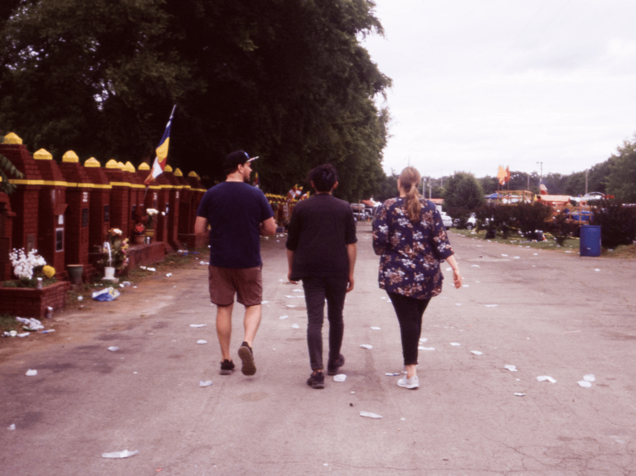 The backs of three friends walking a littered parking lot adjoining a buddhist temple.