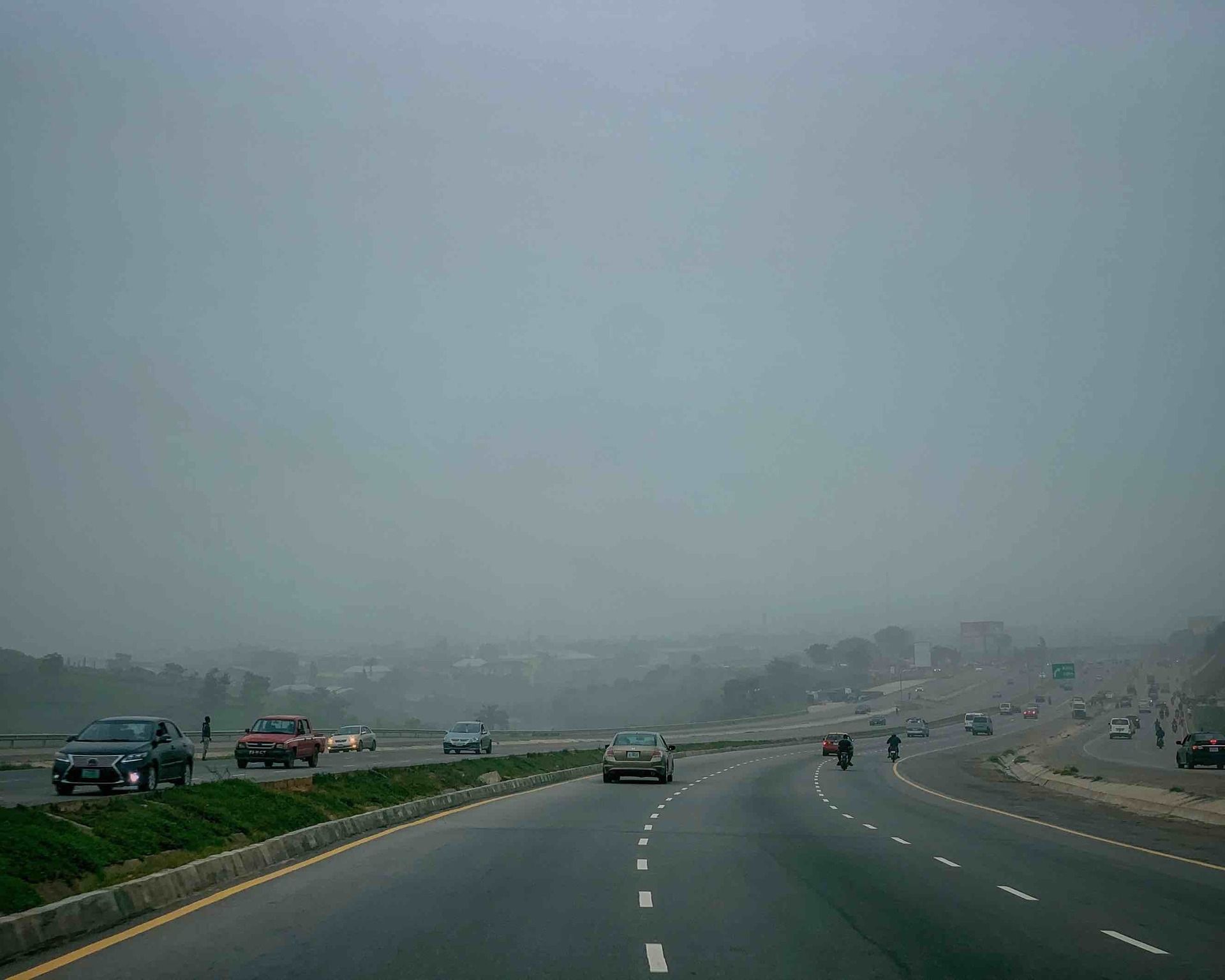 Wide, newly paved lanes of a major Abuja road stretch into settling harmattan haze, captured in late 2023 shortly after the photographer relocating from Lagos—a serene moment of urban transition and dry-season atmosphere on the journey home.