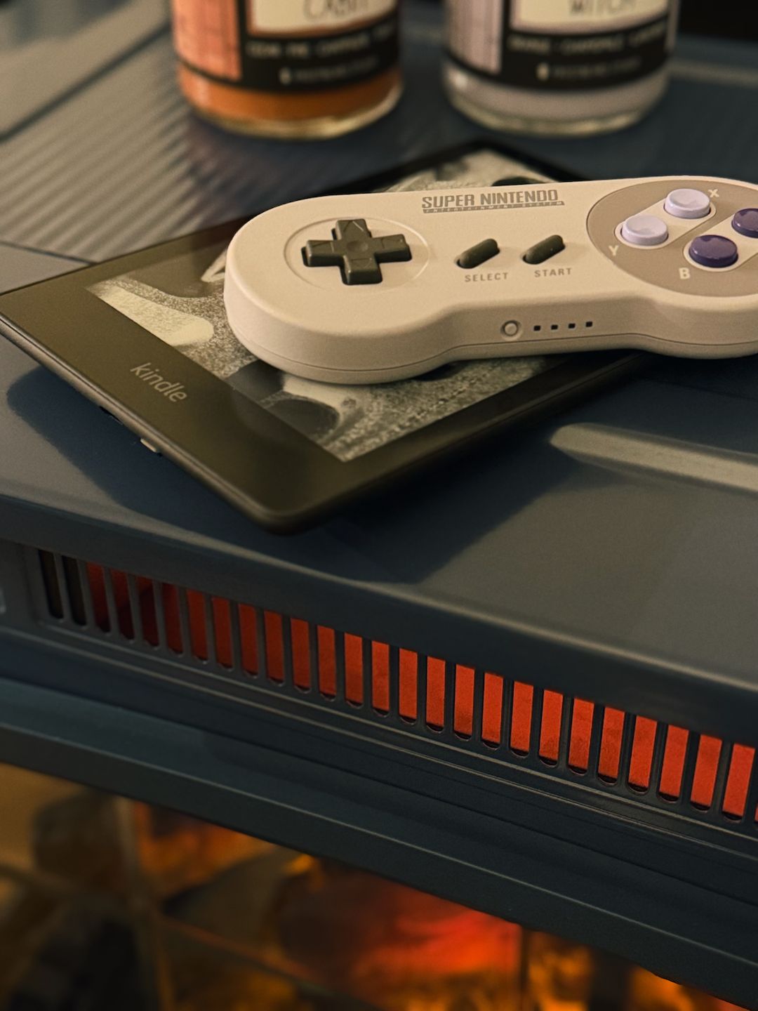 a snes controller, a kindle, and some candles on an infrared fireplace