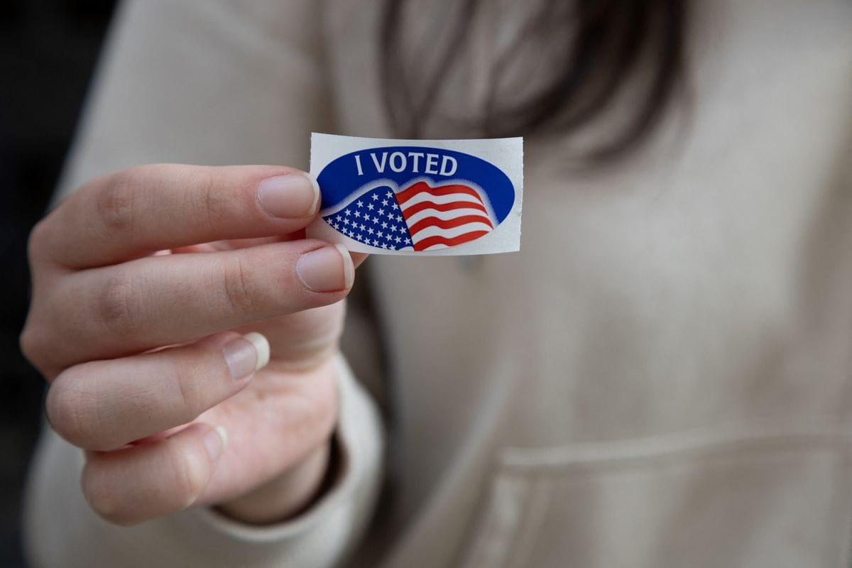 A woman holds an "I voted" sticker in front of her sweatshirt.