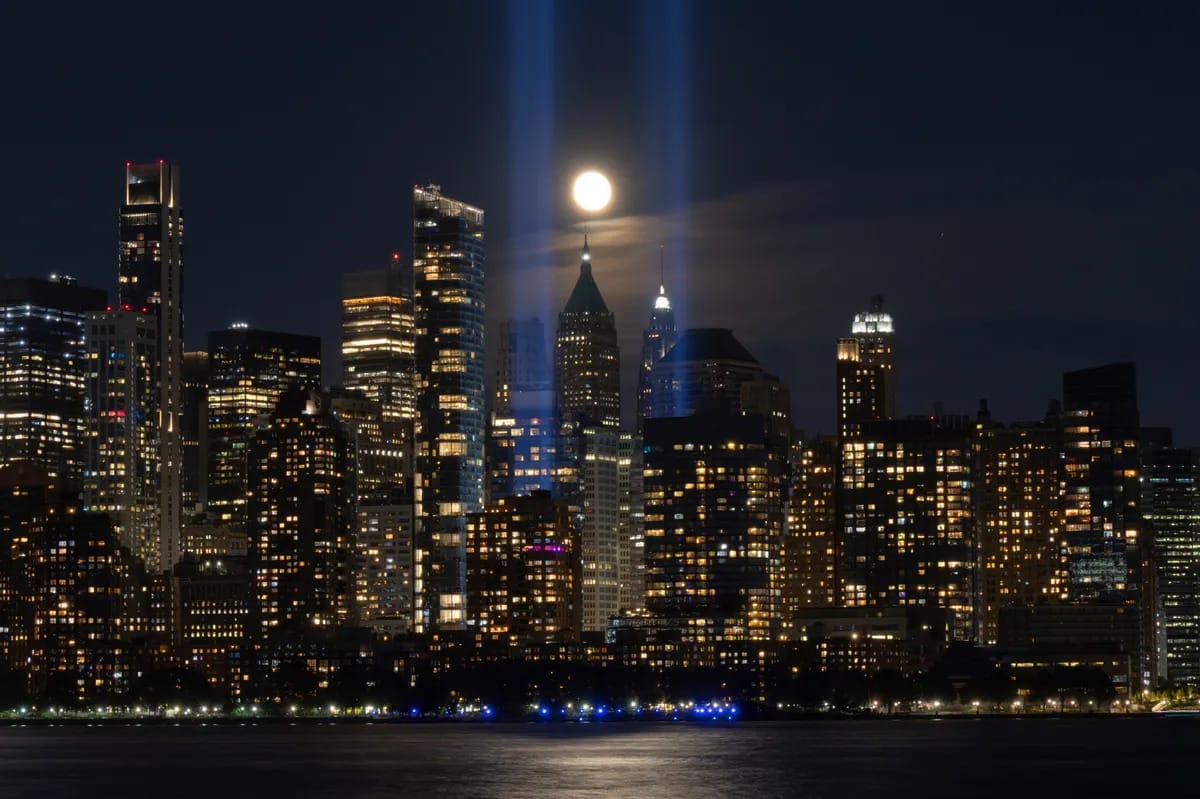 A city is shown at night. The moon appears in the center of the image over the buildings.