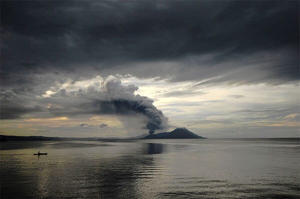 A lone fisherman in Papua New Guinea, casting calmly beneath the erupting Tavurvur volcano.