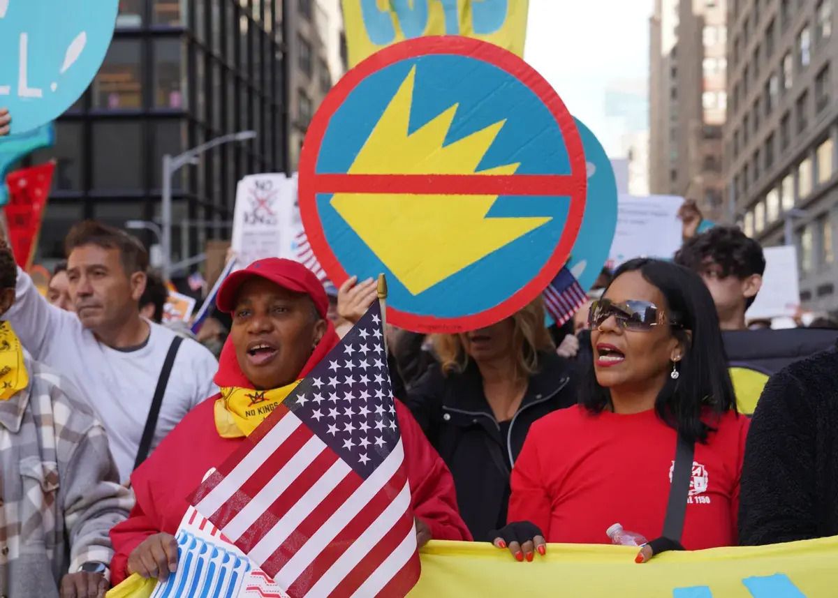A group of people protest outside. You can see large city buildings in the background.