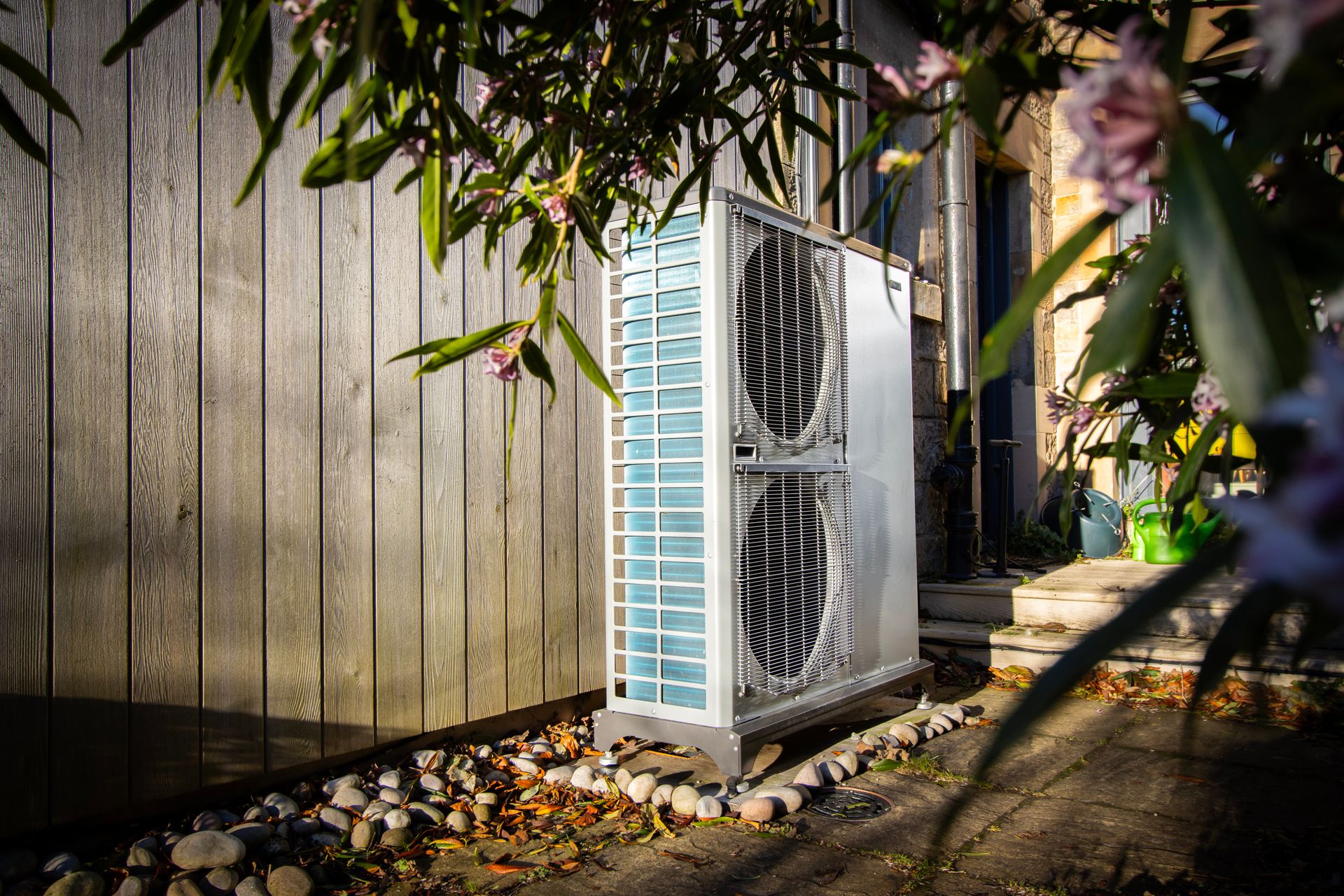 External installation of a Nibe F2040 air source heat pump at a pre-1919 semi-detached sandstone house in Edinburgh. The unit is mounted on a paved area with anti-vibration feet, positioned alongside a timber-clad outbuilding to demonstrate a low-impact heritage retrofit design.