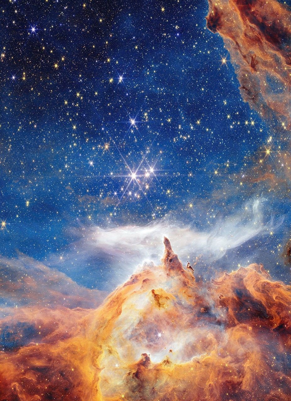 A near-infrared image of the young star cluster Pismis 24, captured by NASA’s James Webb Space Telescope in the heart of the Lobster Nebula, approximately 5,500 light-years away in the constellation Scorpius. The scene reveals thousands of stars at various stages of formation, with the most massive appearing as brilliant points with six-point diffraction spikes. Towering spires of gas and dust, some spanning over 5 light-years, are sculpted by intense radiation and stellar winds from infant stars, triggering new star formation within their dense cores. Cyan hues indicate hot, ionized hydrogen gas; orange traces dust molecules; red marks cooler molecular hydrogen; and black denotes the densest, light-blocking regions. At the center lies Pismis 24-1, once thought to be a single massive star but now known to be a multiple-star system. This image offers a vivid look into the dynamic processes shaping stellar nurseries.