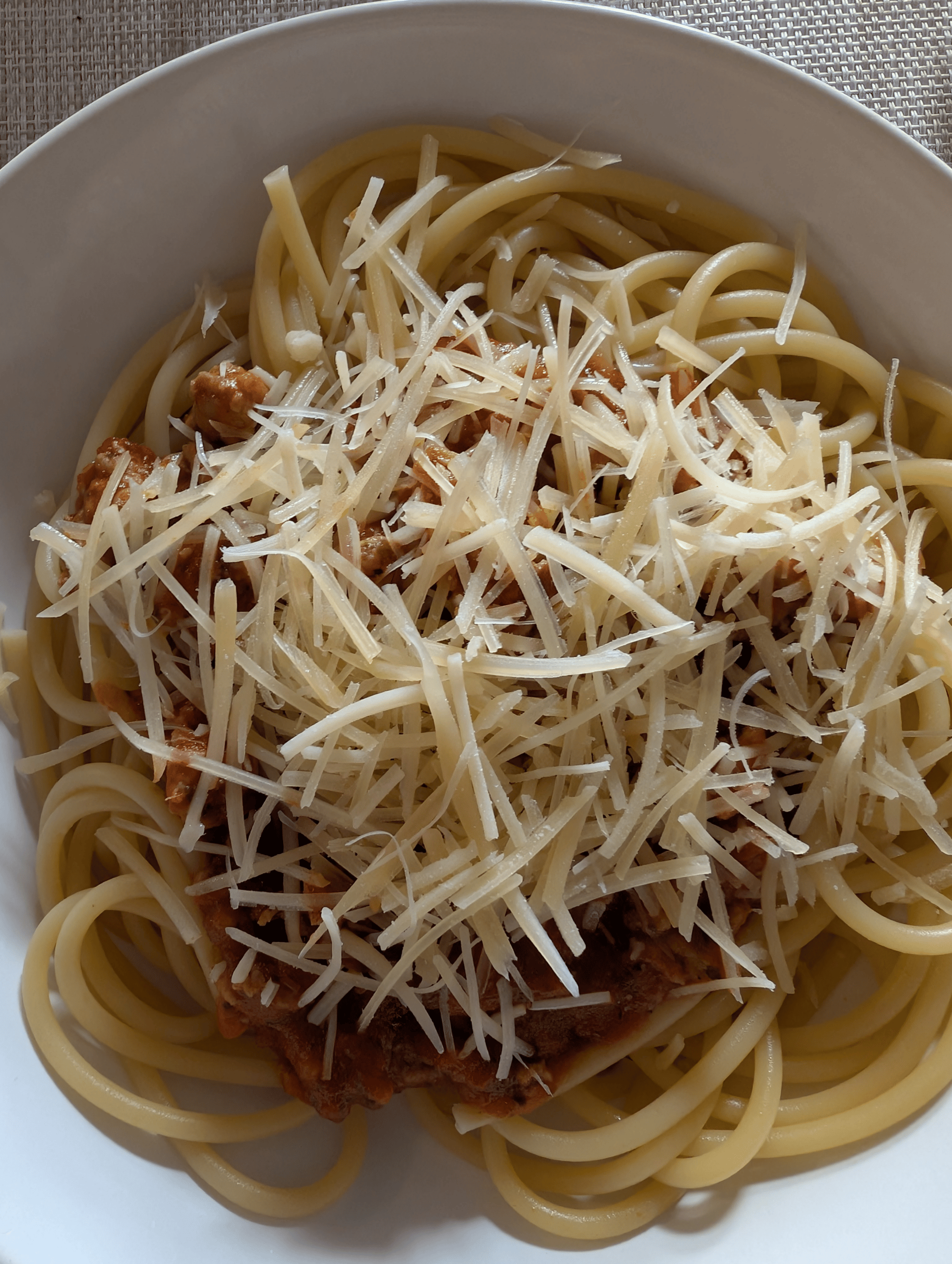 a bowl of bucatini noodles covered in meat sauce and parmesean.