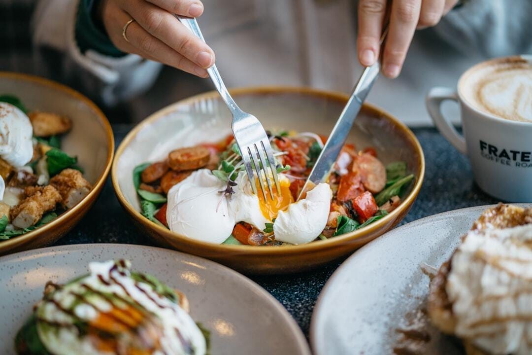 Close up of woman eating breakfast of eggs, sausauge and greens.