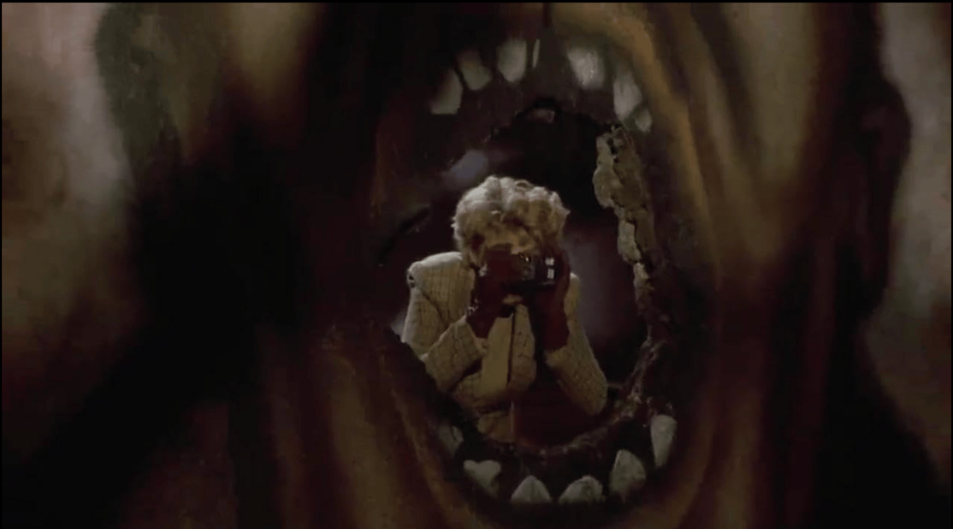 A woman peers through a hole in the wall with a camera. Painted on the wall is a giant face wit the sharp teeth, so it looks like she's inside the mouth. A woman peers through a hole in the wall with a camera. Painted on the wall is a giant face wit the sharp teeth, so it looks like she's inside the mouth.