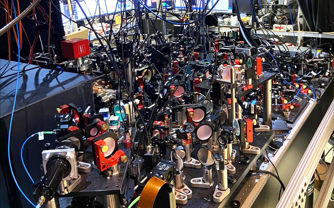 A large table is packed with laser equipment, cables, and optical devices.