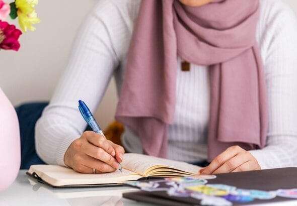 woman sits at table making notes in journal