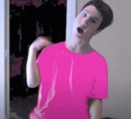 A person in a bright pink shirt stands with one arm raised, mouth open, in a room with a dark background and a white door. The image has a slightly pixelated, animated look.