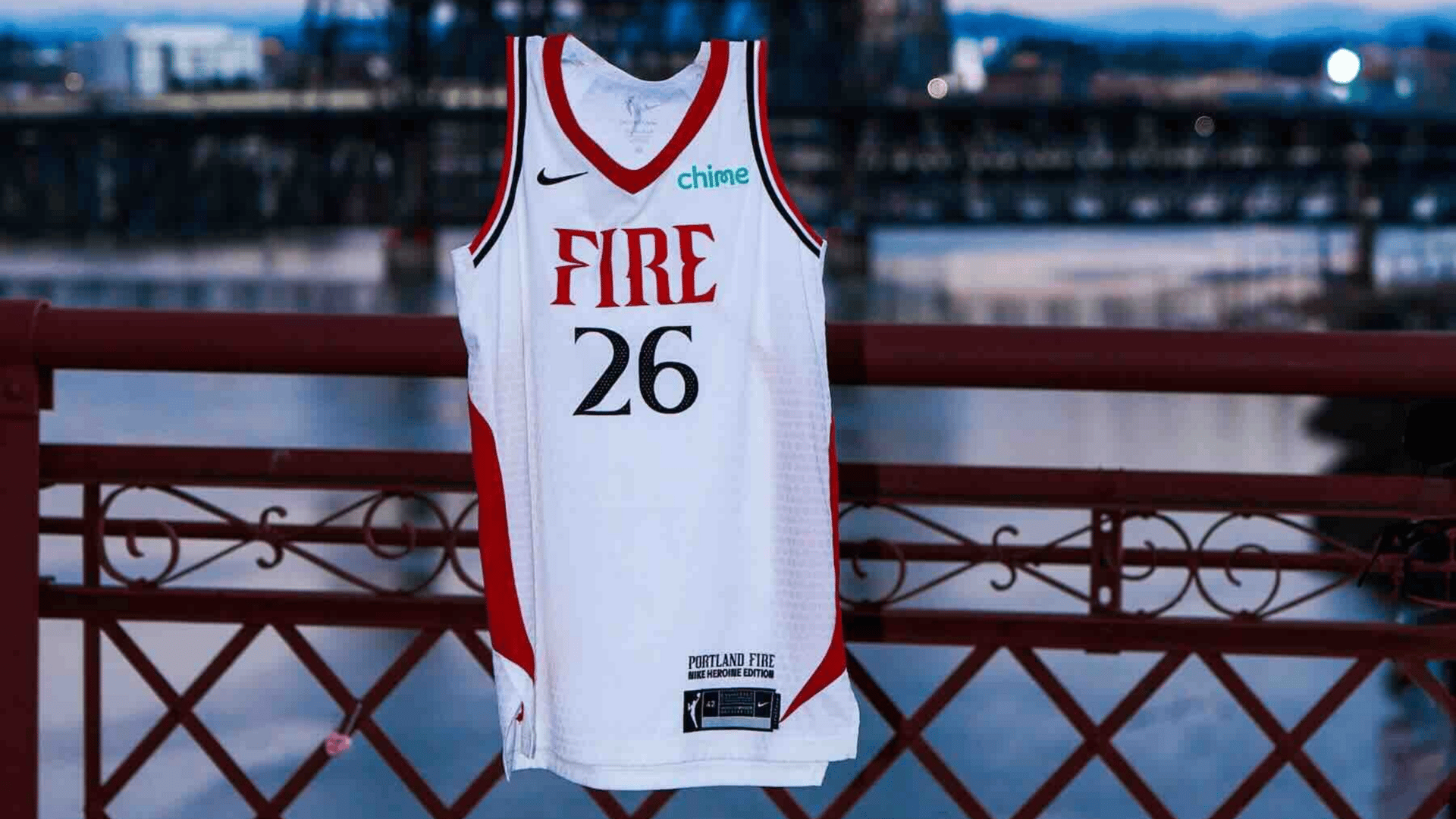 A white and red Portland Fire No. 26 jersey hangs in front of an industrial bridge.