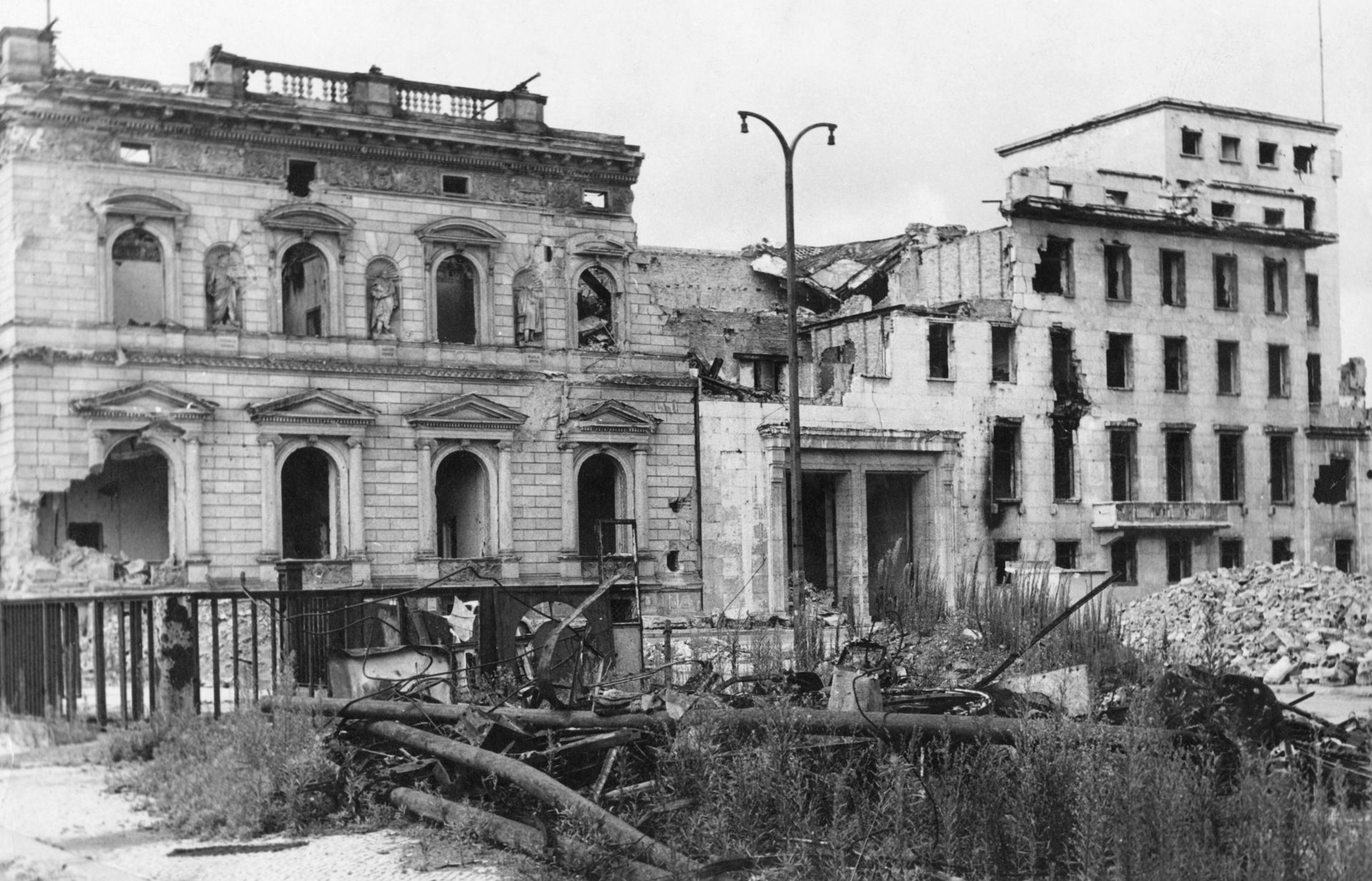 A black and white image shows the ruins of a large white building.