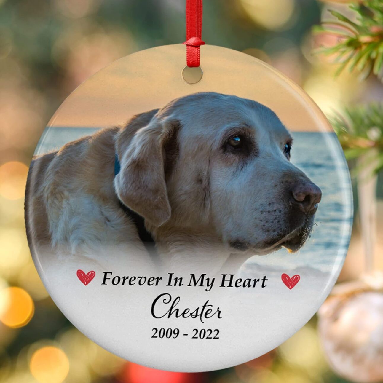 Personalized Pet Christmas Ornament A close-up of a Christmas tree with a custom ornament hanging from a branch, featuring a dog’s name and cartoon image, surrounded by twinkling lights.