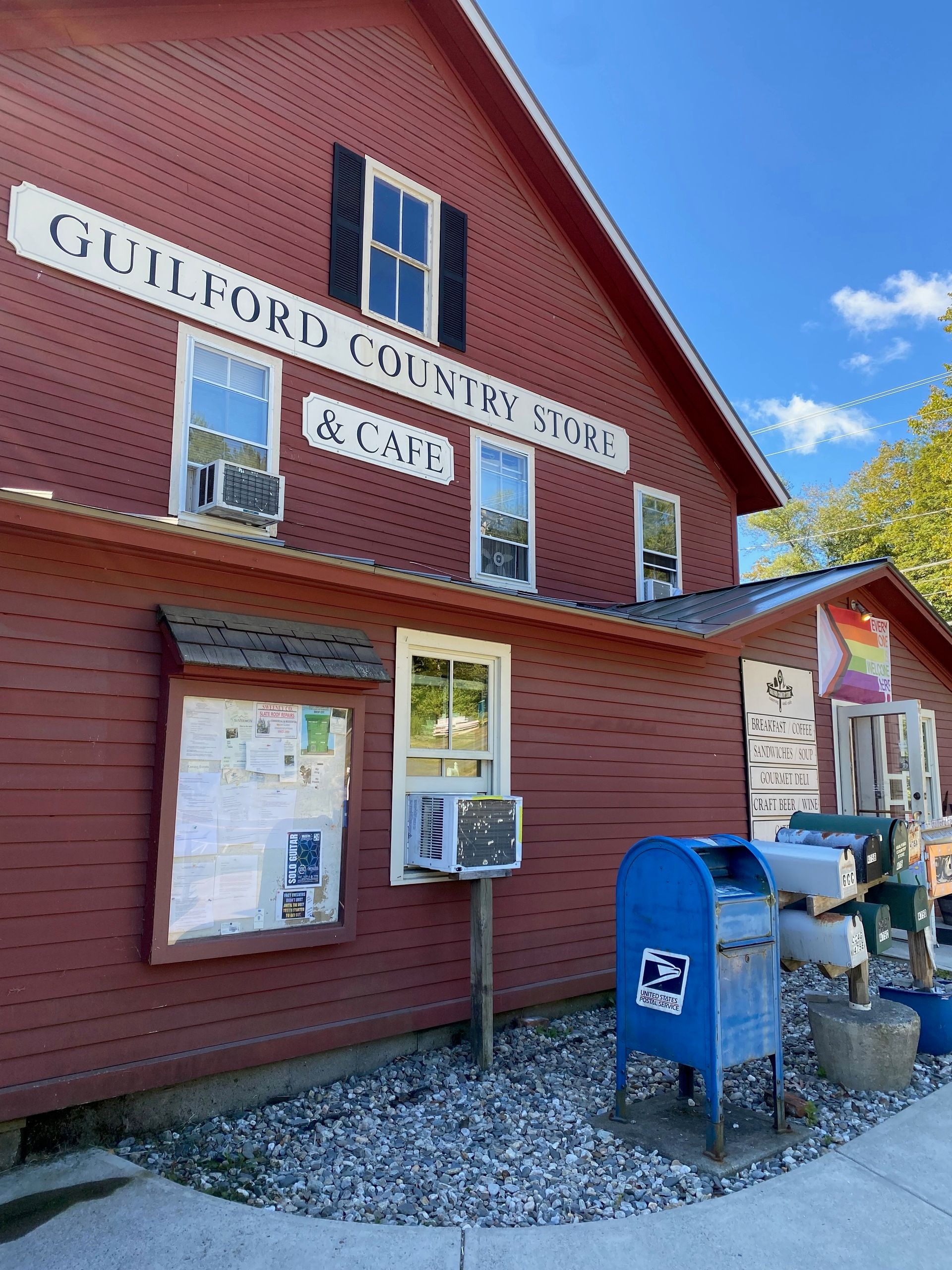 View of the side of the Guilford Country Store, with a message board, mailboxes, and post office box in front.