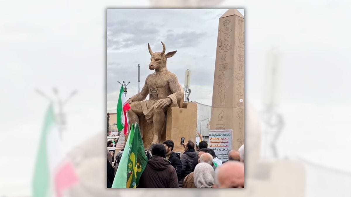 A photo of a large statue of a bull-headed figure sitting on a throne. The Star of David is on its forehead, Baal is written on its chest, and the throne itself has a pentagram and the number 666. An obelisk with hieroglyphs is to the write, and a crowd surrounds with Iranian flags and signs written in Persian. 