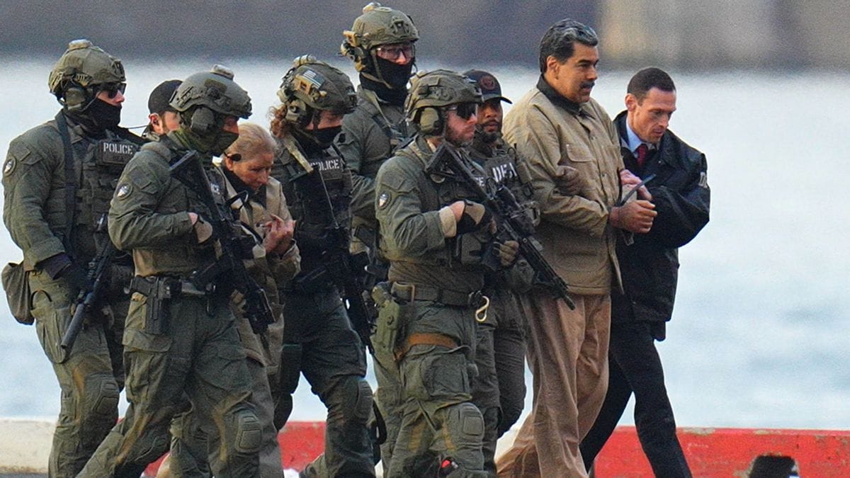 Photo of a Latino man being escorted by several U.S. military personnel wielding long guns
