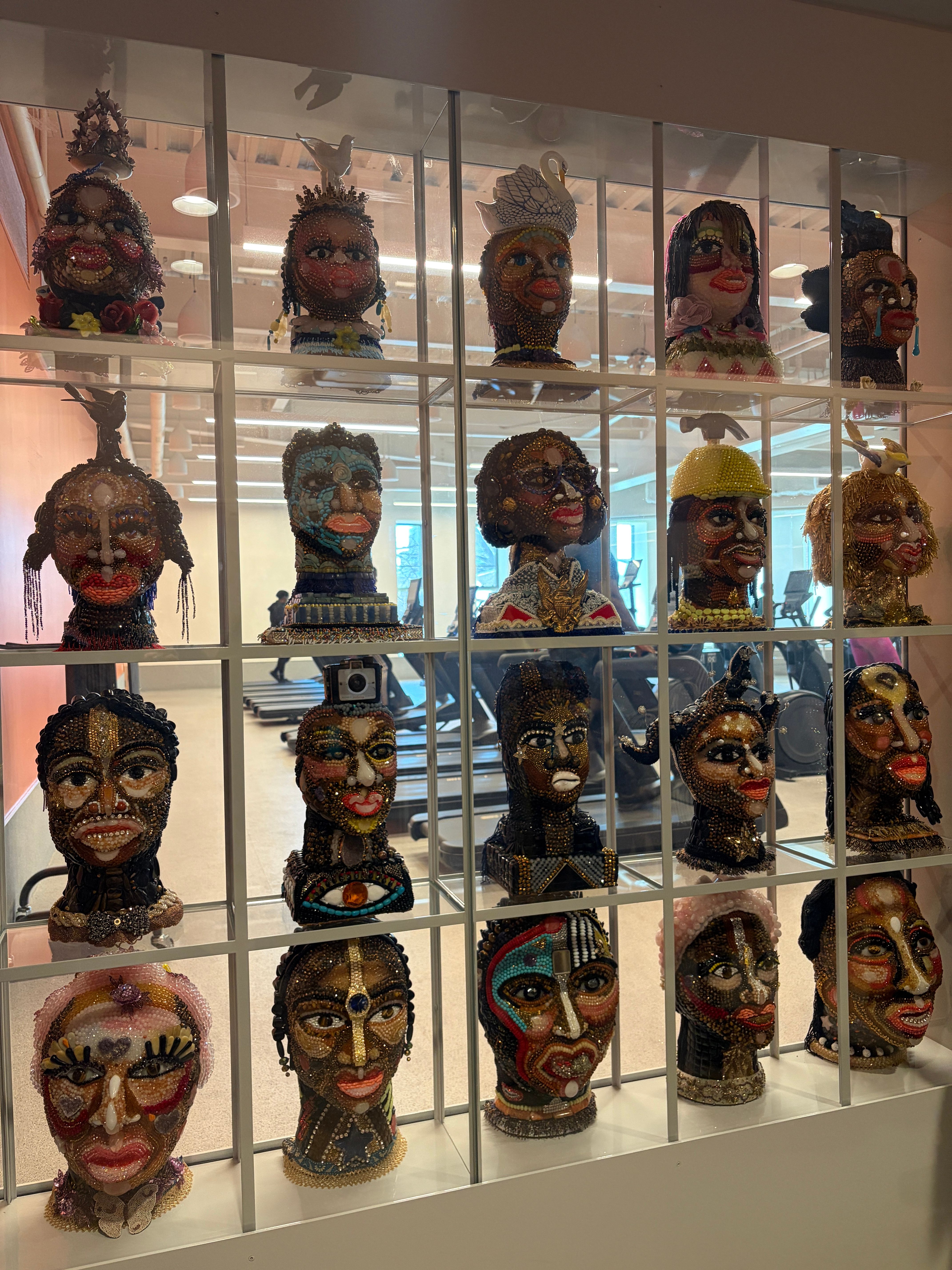 A glass vitrine holding a grid of 25 portrait busts of Black neighbors and celebrities by artist vanessa german