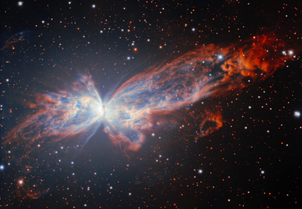 An image of a dramatic cloud of gas shaped vaguely like a butterfly, with bluish gas on the inside of the “wings” surrounded by redder gas.