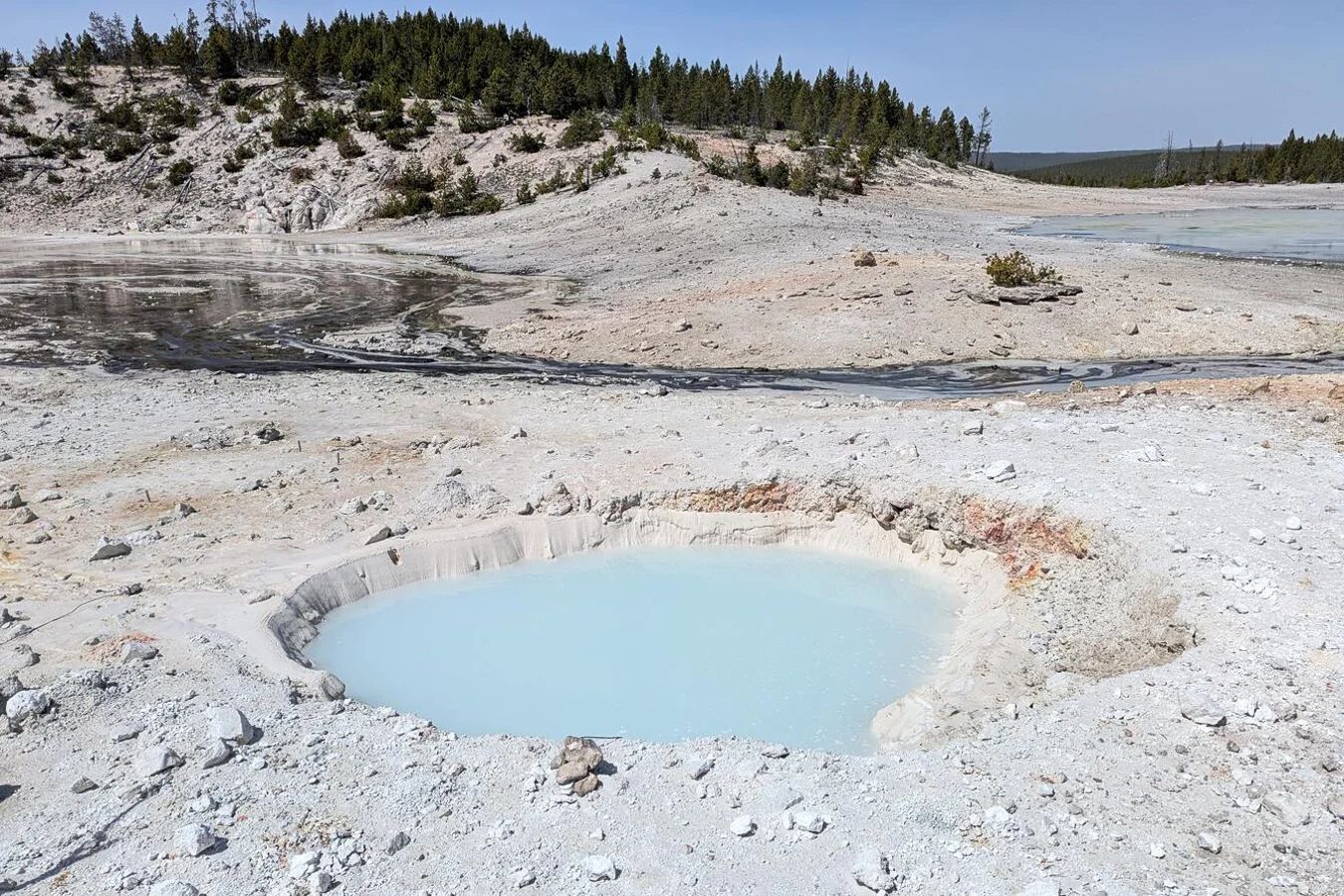A roughly circular, pale blue pool in a landscape of white sand and rock.