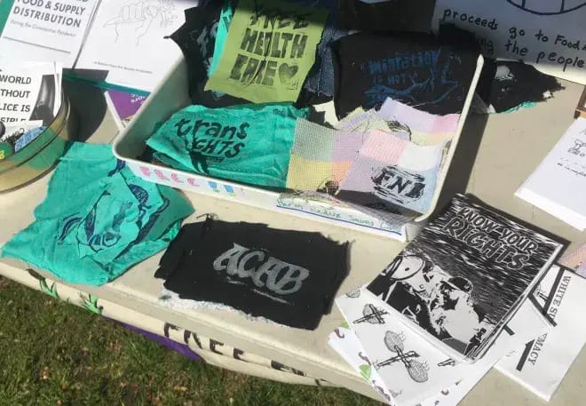 A photo of patches laid out on a table. Some read "Trans Rights" "ACAB" and "FNB"