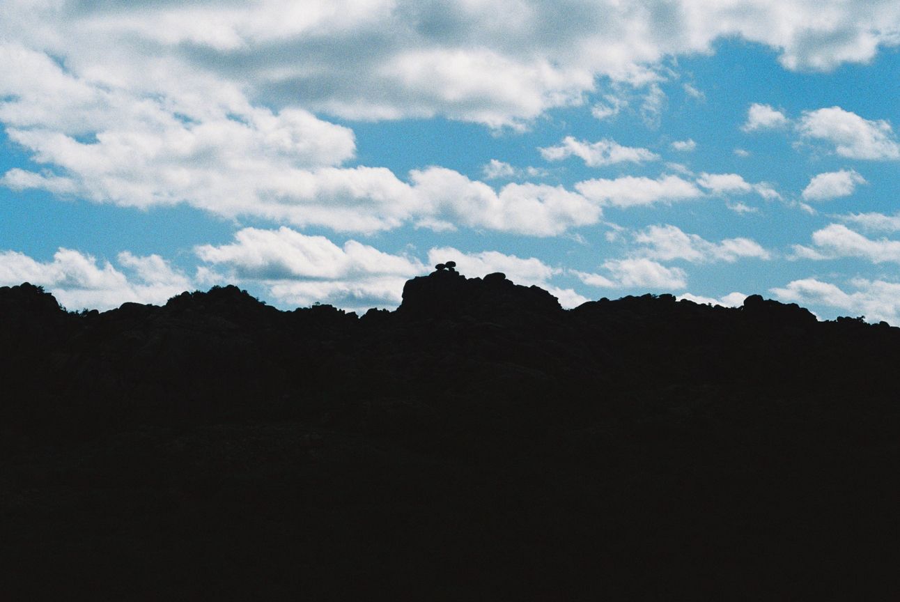 Two rocks that look like eyes are silhouetted against a blue sky with puffy white clouds dotted across it.