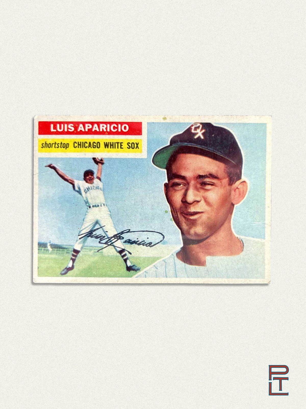 A vintage baseball card featuring Luis Aparicio of the Chicago White Sox. The card includes two images: one of Aparicio in a white “Chicago” uniform mid-throw on a sunny field, and another of him smiling in a close-up portrait while wearing a black White Sox cap with the classic “Sox” logo. His name appears in bold red and white at the top left, with “shortstop” and “Chicago White Sox” beneath it in yellow. A facsimile autograph of Aparicio is printed across the card. The background is a soft, neutral gray, with the Pine Tar Letter “PTL” logo in the bottom-right corner.