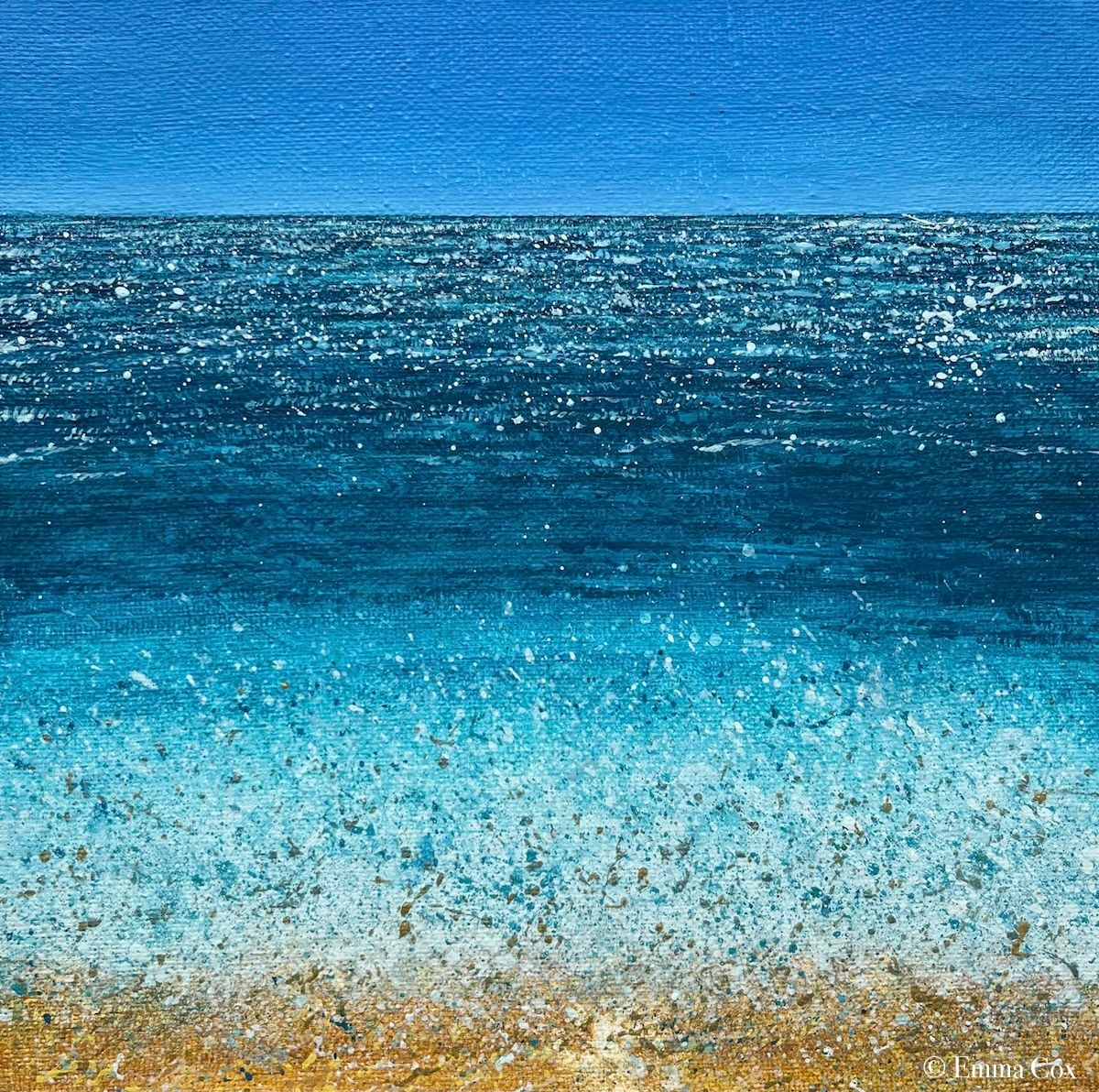 A seascape with a wave crashing on the sandy shoreline. The horizon is clear blue sky. The sun glitters on the water.