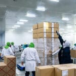 Latino Workers Packing And Securing Cardboard Boxes At A Food Pr