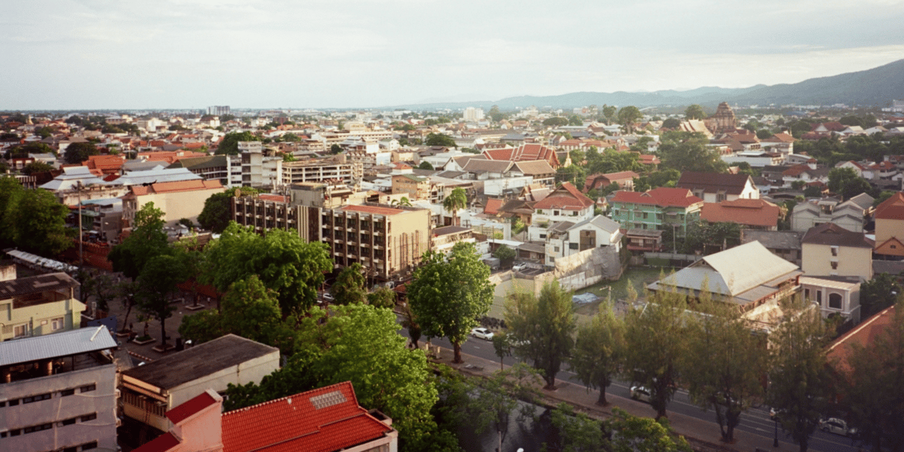 A vista overlooking Chiang Mai City. Roads, low buildings, and temples spread to the horizon where mountains rise.