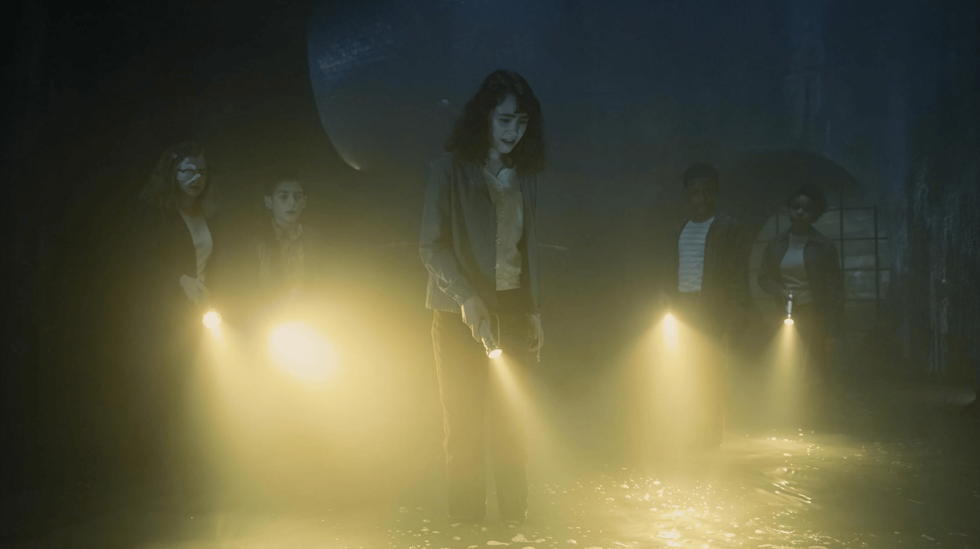 A group of five children stand in the dark sewers with flashlights.