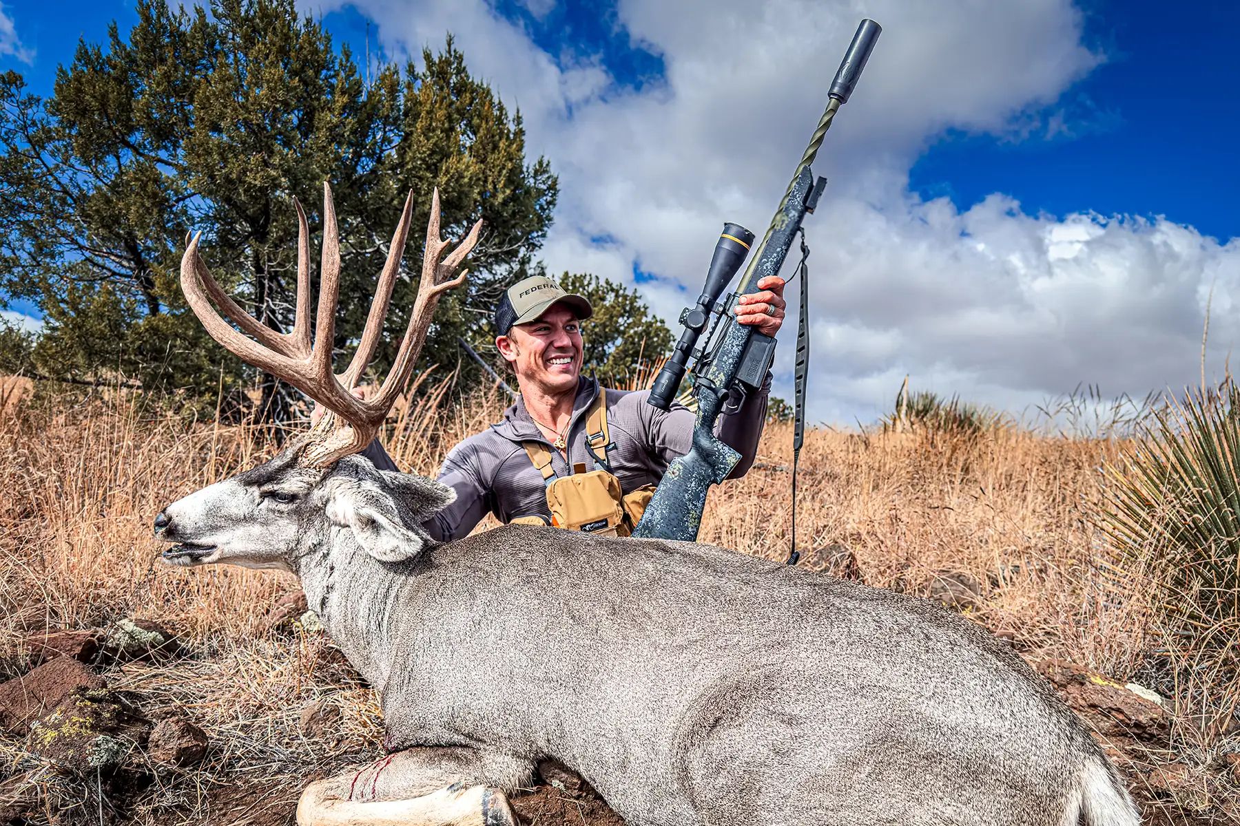 man with a rifle and a mule deer buckk