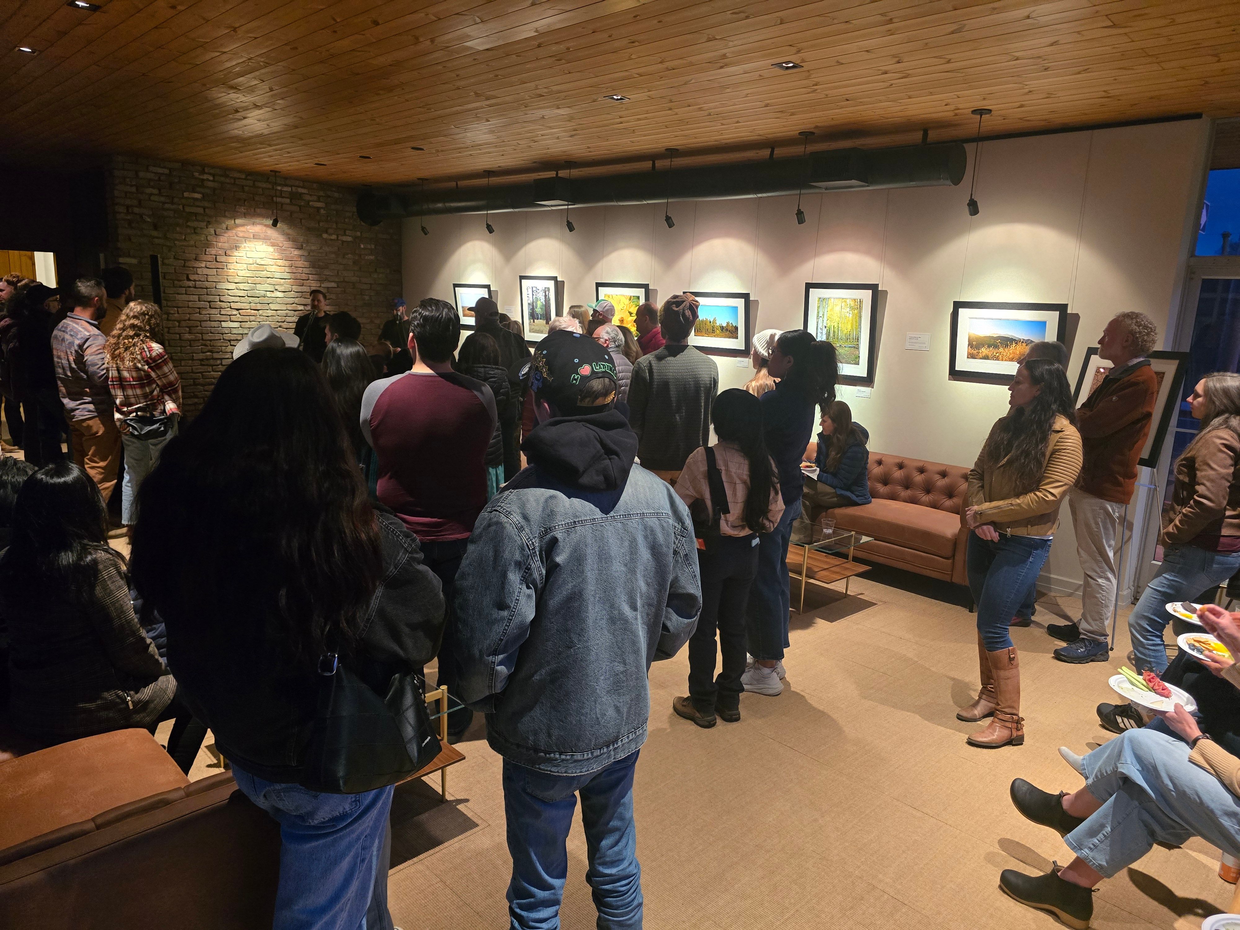 A local group listens to a speaker in a comfortable community space with a wood ceiling, modern looking couches, and nature photography displayed on the wall.