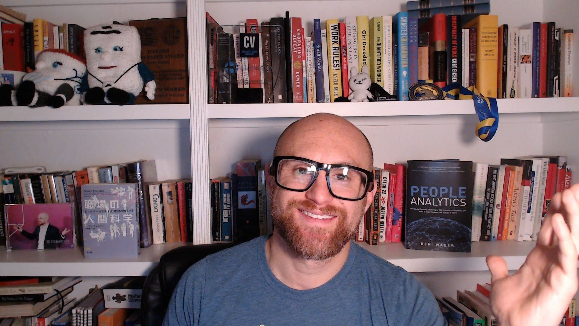 A selfie of me in front of my packed white bookshelves. I'm a bald, middle-aged, white man with a red beard flecked with white. I'm wearing glasses with thick black rims and a dark aqua colored t-shirt.