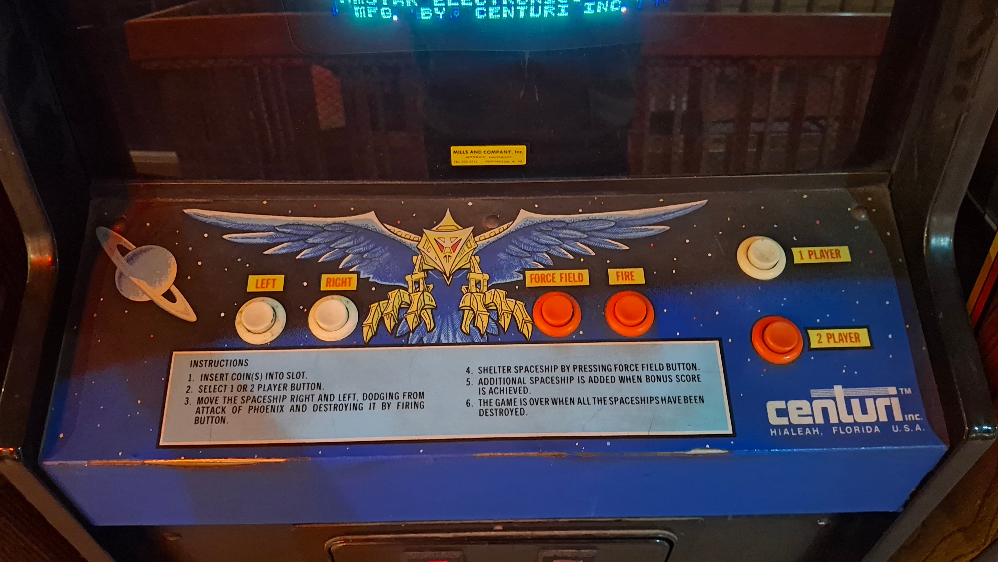 A photo of the inputs on Centuri's Phoenix cabinet, with white Left and Right buttons on the left, and red Force Field and Fire buttons on the right. In between is art of one of the bird-like spaceships you will be fighting.