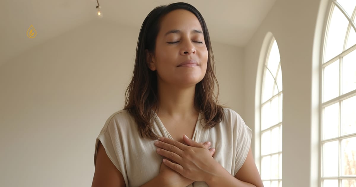 Jenice Story seated with eyes closed and hands on heart in a softly lit room, representing calm, grounding, and nervous system regulation.