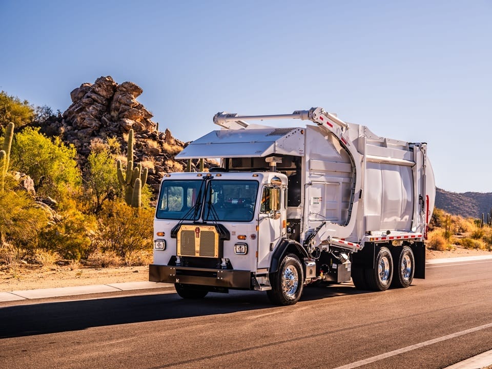 Kenworth cab-over front loader garbage truck driving through desert highway, used for commercial front waste collection routes.