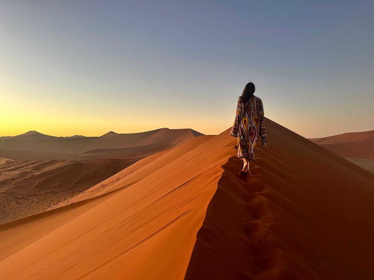 Image of a figure walking along the top of a sand dune, with the sunrise in the distance, evocative of possibilities