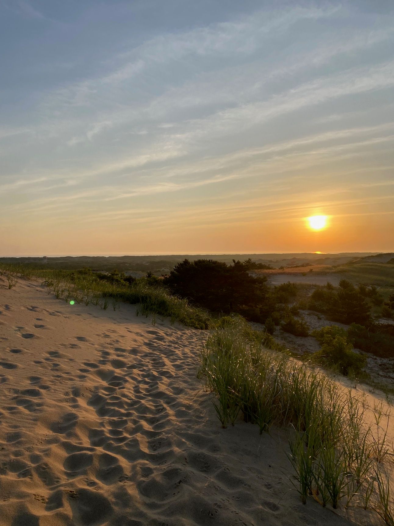 The sun rising over the dunes, a path of footprints alongside one. 
