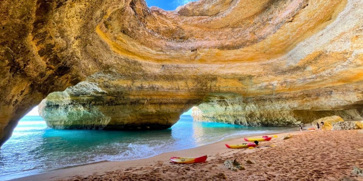 Sunlight streaming into a sea grotto with crystal-clear water and a kayak floating near the entrance