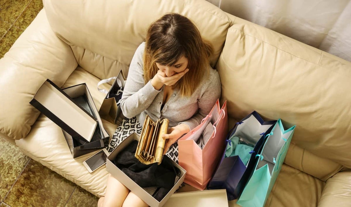 woman sitting on couch with shopping bags looking at her empty wallet