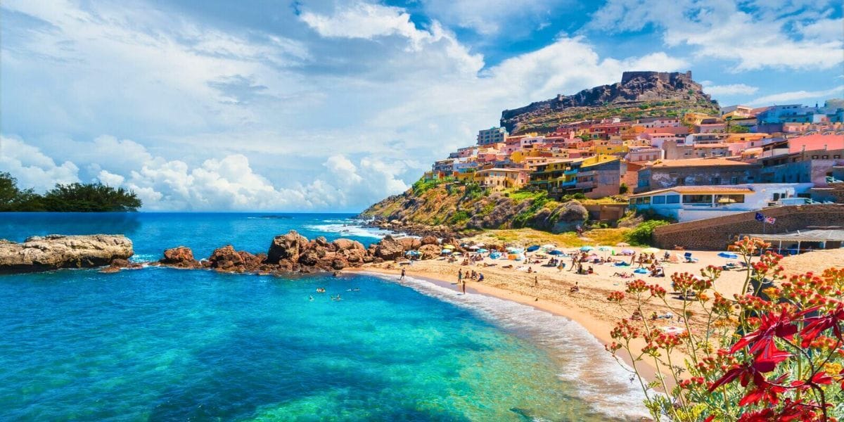 Scenic village in Sardinia with pastel buildings, mountain backdrop, and locals walking along cobblestone streets