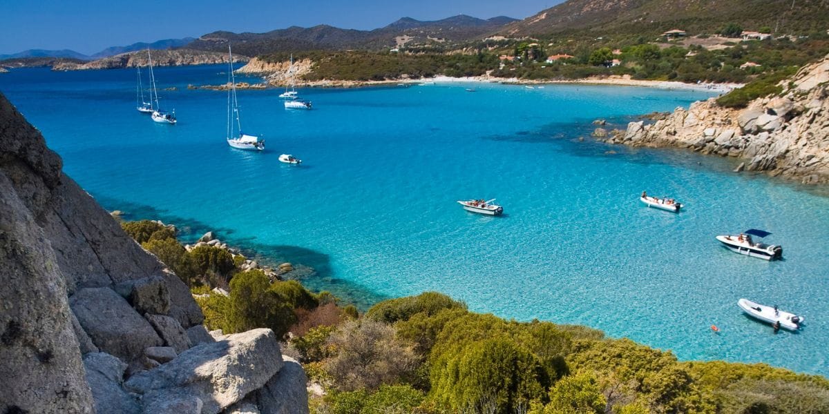 Secluded white-sand crescent beach surrounded by pine and juniper trees, with clear aquamarine water