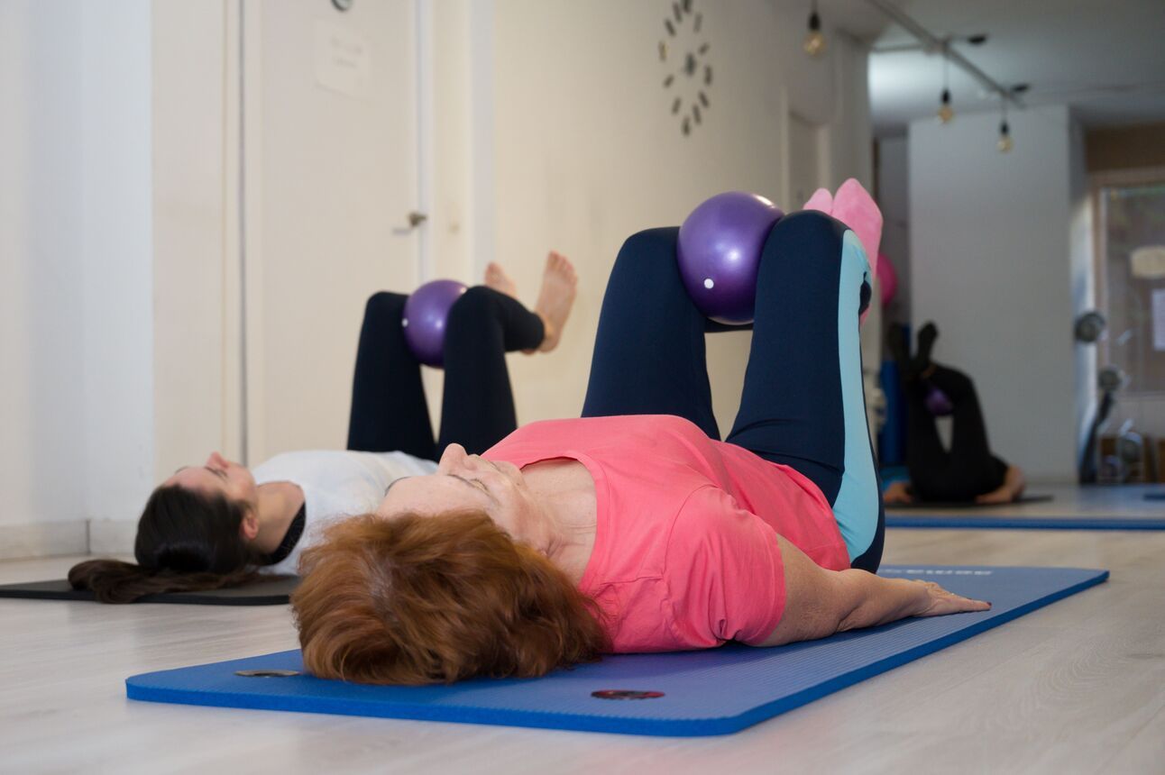 Two women laying on mats with a small weighted ball between their knees, which they are floating above them