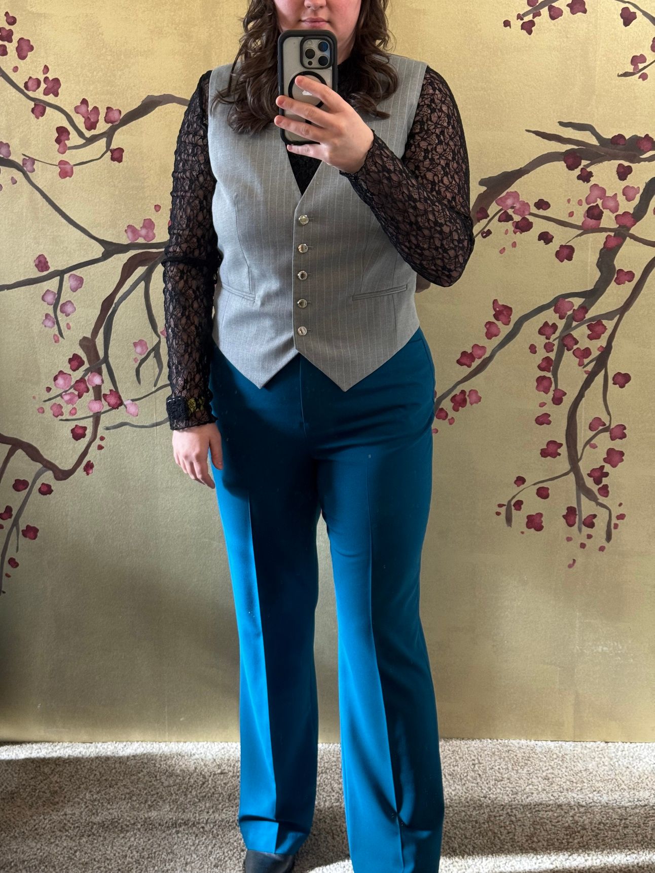 photo of a femine body in black lace top, pinstripe vest, and blue slacks.