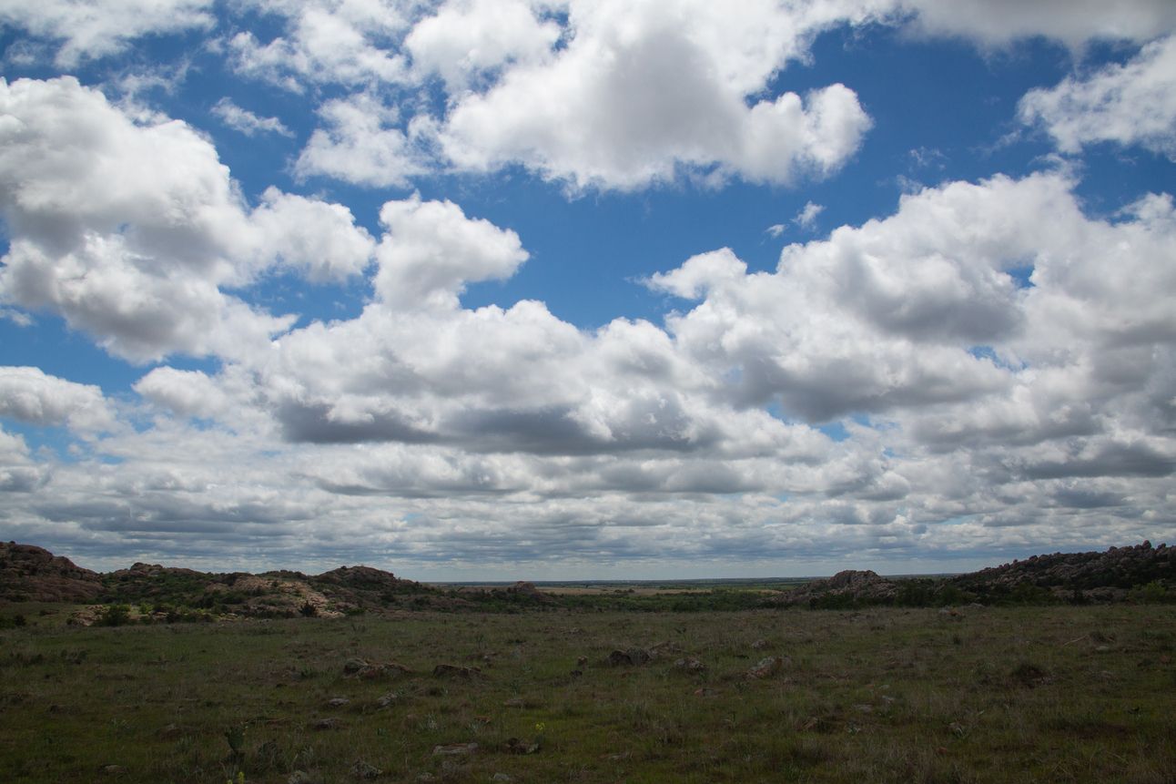 A blue sky filled with white puffy clouds over a wide green vista.
